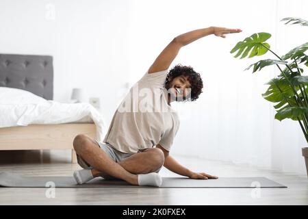 Sportlicher indischer Mann, der zu Hause Yoga praktiziert und sich dehnt Stockfoto
