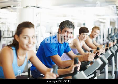 Start auf den Heimtrainern. Eine Reihe von Leuten, die im Fitnessstudio an den Heimtrainern trainieren. Stockfoto