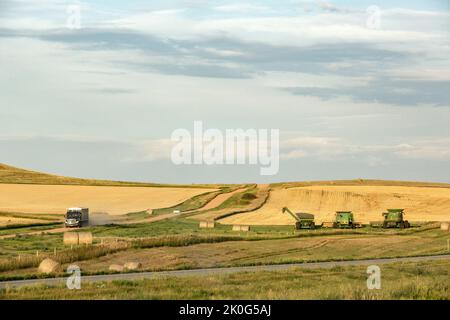 Great Plains Landschaft mit einer ländlichen Schotterstraße, Getreidewagen, landwirtschaftlichen Maschinen und geernteten Weizenfeldern auf den sanften Hügeln des westlichen North Dakota Stockfoto