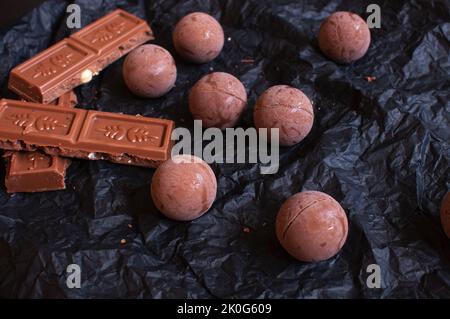 Schokoladen-Bonbons mit Schokoladenstücken auf dunklem zerknittertem Bastelpapier mit Lavendelblüten Stockfoto