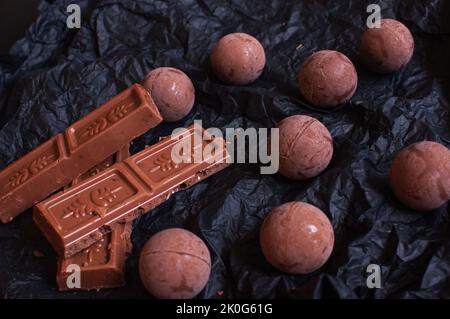 Schokoladen-Bonbons mit Schokoladenstücken auf dunklem zerknittertem Bastelpapier mit Lavendelblüten Stockfoto