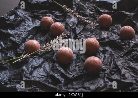 Schokoladen-Bonbons auf dunklem zerknittertem Bastelpapier mit Lavendelblüten Stockfoto