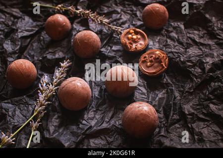 Schokoladen-Bonbons auf dunklem zerknittertem Bastelpapier mit Lavendelblüten Stockfoto