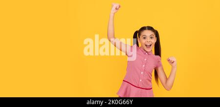 Fühlen Sie sich wie ein Gewinner. Glücklicher Sieger gelber Hintergrund. Fröhliches Kind schreit, was eine Geste des Gewinnens macht. Kindergesicht, horizontales Poster, Teenager-Mädchen isoliert Stockfoto