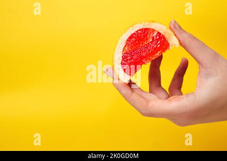 Defokussieren Sie die weibliche Hand mit einem Stück einer roten Grapefruit. Gesundes Lebensmittelkonzept. Frischer Orangensaft. Veganes, vegetarisches Konzept. Banner mit Kopierbereich. Ci Stockfoto