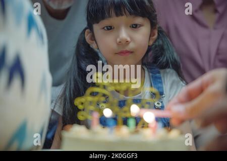 Geburtstagsüberraschung. Glückliche asiatische Familie Großeltern und Mutter feiern genießen Geburtstagsfeier mit Kuchen der Enkelin zu Hause in der Nacht Stockfoto
