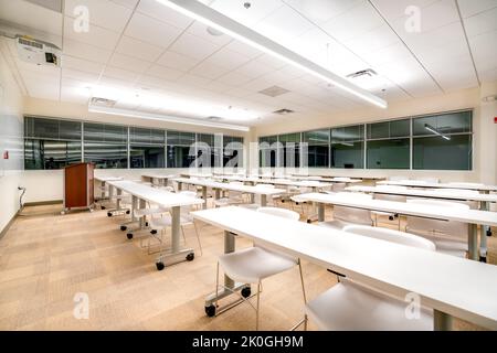 Beispiel für eine neue, leere, unscheinbare Büroschulung, einen Besprechungsraum mit Schreibtischen, Stühlen und Whiteboard. Das Zimmer könnte sich in fast jedem Bürobereich befinden. Stockfoto