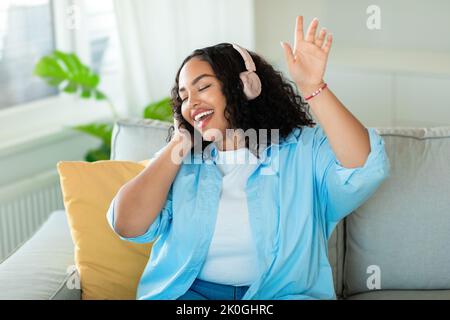 Afrikanische Frau Trägt Kopfhörer Singen Mit Geschlossenen Augen Zu Hause Stockfoto