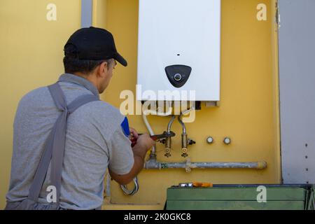 Klempner auf einer Leiter mit einem Schraubenschlüssel während der Reparatur und Wartung eines Gaskessels in Erwartung des Winters. Ersetzen eines Heim-Zentralheizung Sanitär Stockfoto