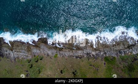 Luftaufnahme von Meereswellen, die auf Felsen in den blauen Ozean krachen. Blick von oben auf die Küstenfelsen im Ozean von Phuket. Landschaftspunkt von Laem Phromthep Stockfoto