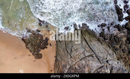 Luftaufnahme von Meereswellen, die auf Felsen in den blauen Ozean krachen. Blick von oben auf die Küstenfelsen im Ozean von Phuket. Landschaftspunkt von Laem Phromthep Stockfoto