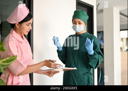 Eine professionelle asiatische Chirurgen oder Neurologe, die mit einer Krankenschwester diskutiert und die Aufzeichnungen eines Patienten mit Medikamentenanamnese und die aktuelle Diagnose überprüft Stockfoto