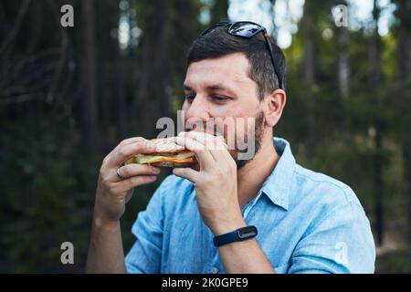 Ein junger Mann isst ein Sandwich in der Natur. Vorderansicht. Stockfoto