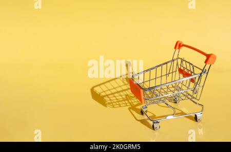 Kleiner Supermarkt Lebensmittelgeschäft Push Cart zum Einkaufen. Shopaholic. Käufer. Einkaufskonzept. Nahaufnahme. Isolierter Einkaufswagen auf gelbem Hintergrund. Cop Stockfoto