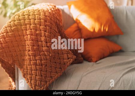 Orangefarbene Kissen und ein braunes kariert auf einem grauen Sofa Stockfoto