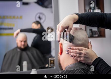 Die Hände des jungen Barbiers machen Haarschnitt zu attraktiven Mann in Friseurladen. Rasieren Sie Ihre Glatze Kopf Stockfoto