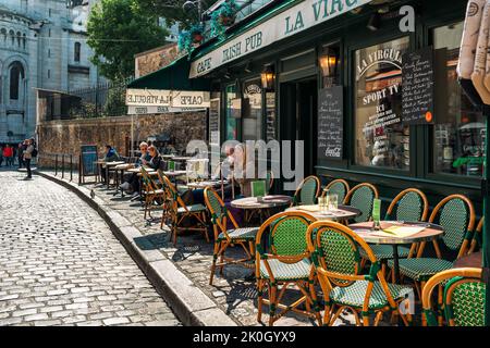 Menschen, die Kaffee trinken, werden in einem typischen Café im Freien mit alten Stühlen und Tischen auf dem Bürgersteig der gepflasterten Straße in Paris, Frankreich, serviert. Stockfoto