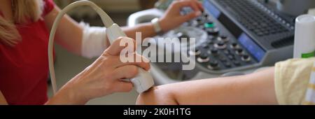 Der Arzt führt in der Klinik eine Ultraschalluntersuchung des Ellenbogens des Patienten durch Stockfoto