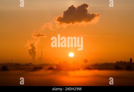 Sehnde, Deutschland. 12. September 2022. Die Sonne geht neben dem Kraftwerk Mehrum im Bezirk Peine auf und färbt den Morgennebel in warmes Licht. Das Kohlekraftwerk ist seit August als erster „Marktrückkehrer“ wieder am Netz. Eine Verordnung erlaubt es, Kohlekraftwerke aus der sogenannten Netzreserve wieder in Betrieb zu nehmen, um Erdgas zu sparen. Quelle: Julian Stratenschulte/dpa/Alamy Live News Stockfoto