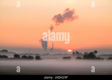 Sehnde, Deutschland. 12. September 2022. Die Sonne geht neben dem Kraftwerk Mehrum im Bezirk Peine auf und färbt den Morgennebel in warmes Licht. Das Kohlekraftwerk ist seit August als erster „Marktrückkehrer“ wieder am Netz. Eine Verordnung erlaubt es, Kohlekraftwerke aus der sogenannten Netzreserve wieder in Betrieb zu nehmen, um Erdgas zu sparen. Quelle: Julian Stratenschulte/dpa/Alamy Live News Stockfoto