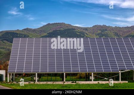 Viele Sonnenkollektoren auf dem Feld. Horizontale Ausrichtung, blauer Himmel, graue Tafeln, Berg im Hintergrund Stockfoto