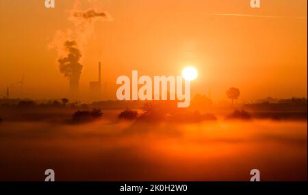 Sehnde, Deutschland. 12. September 2022. Die Sonne geht neben dem Kraftwerk Mehrum im Bezirk Peine auf und färbt den Morgennebel in warmes Licht. Das Kohlekraftwerk ist seit August als erster „Marktrückkehrer“ wieder am Netz. Eine Verordnung erlaubt es, Kohlekraftwerke aus der sogenannten Netzreserve wieder in Betrieb zu nehmen, um Erdgas zu sparen. Quelle: Julian Stratenschulte/dpa/Alamy Live News Stockfoto