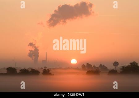 Sehnde, Deutschland. 12. September 2022. Die Sonne geht neben dem Kraftwerk Mehrum im Bezirk Peine auf und färbt den Morgennebel in warmes Licht. Das Kohlekraftwerk ist seit August als erster „Marktrückkehrer“ wieder am Netz. Eine Verordnung erlaubt es, Kohlekraftwerke aus der sogenannten Netzreserve wieder in Betrieb zu nehmen, um Erdgas zu sparen. Quelle: Julian Stratenschulte/dpa/Alamy Live News Stockfoto