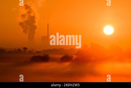 Sehnde, Deutschland. 12. September 2022. Die Sonne geht neben dem Kraftwerk Mehrum im Stadtteil Peine auf und färbt den frühen Morgennebel in ein warmes Licht. Das Kohlekraftwerk ist seit August als erster „Marktrückkehrer“ wieder am Netz. Eine Verordnung erlaubt es Steinkohlekraftwerken aus der sogenannten Netzreserve, wieder in Betrieb zu nehmen, um Erdgas zu sparen. Quelle: Julian Stratenschulte/dpa/Alamy Live News Stockfoto