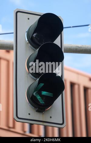 Nahaufnahme einer Ampel, die an einem sonnigen Tag ein grünes Licht für Autos zeigt, die links von der Straße abbiegen Stockfoto