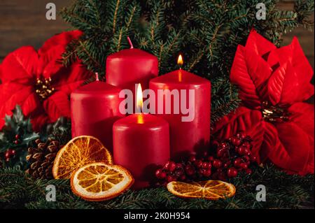 Zwei brennende rote Adventskerzen in Adventskranz-Dekoration auf dunklem Holzhintergrund. Tradition in der Zeit vor Weihnachten. weihnachtslichter mit weihnachtlicher Tannendeko-Hintergrundkonzept. Festliches Stillleben. Stockfoto