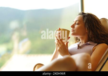 Frau sitzt auf einem Stuhl und trinkt Kaffee zu Hause Stockfoto