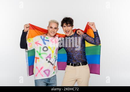 Aufgeregter schwuler Mensch und glücklicher Schwuler mit lgbt-Flagge und Blick auf die Kamera isoliert auf grauem, Stock-Bild Stockfoto