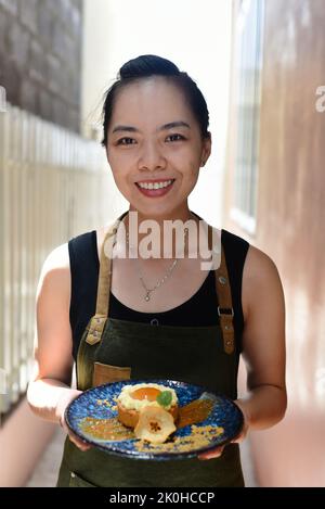 Vietnamesische Kellnerin in Schürze mit Apfelkuchen auf einem blauen Teller Stockfoto