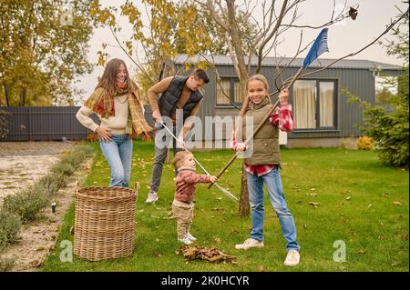 Die ganze Familie putzt den Hof mit Gartenrechen Stockfoto