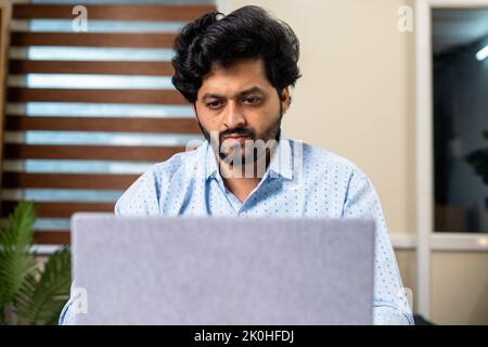 Vorderansicht des Mitarbeiters oder Unternehmers eines Unternehmens, der ernsthaft am Laptop im Büro arbeitet – Konzept der fokussierten, durchdachten und Problemlösung Stockfoto