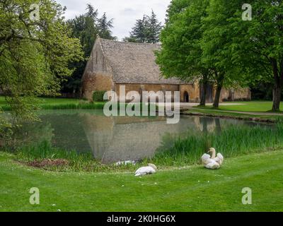 Ein Blick auf die mittelalterliche Tithe Barn von der anderen Seite des Ententeiches, Stanway House, Gloucestershire, Großbritannien; jetzt als Hochzeitslocation genutzt Stockfoto