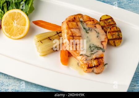 Gegrillter Lachs in Sauce mit Gemüse und Kartoffeln auf einem weißen Porzellanteller Stockfoto