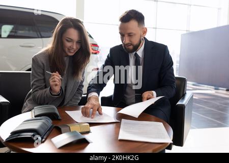 Junge Frau kauft ein neues Auto in einem Autohaus und unterzeichnet Dokumente, Kfz-Versicherung Konzept Stockfoto