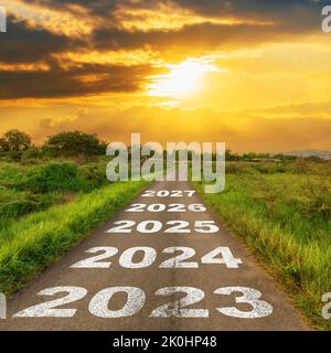 Leere Asphaltstraße und Konzept für das neue Jahr 2023. Fahrt auf einer leeren Straße nach 2023 mit Sonnenuntergang. Stockfoto