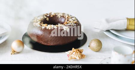 Großer runder Schokoladenmandelkuchen auf dem Tisch mit Silvesterteller, weihnachtlich weißer skandinavischer Festtafel Stockfoto