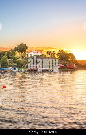 Ein kleines Häuschen mit Booten im Fluss bei Sonnenuntergang in Henan, Orust, Schweden. Stockfoto