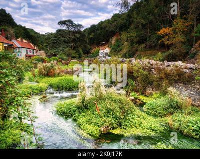 Der Fluss Cheddar Yeo fließt von der Cheddar Gorge in das Dorf. Das Cheddar Yeo Schwert liegt im Vordergrund mit den Soay Schafstatuen dahinter. Stockfoto