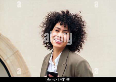 Porträt einer stilvollen Frau mit drahtlosen Ohrhörern lächelnd glücklich Blick auf die Kamera mit ihrem Telefon in der Hand, Konzept der Jugend und Technologie, Kopie Stockfoto
