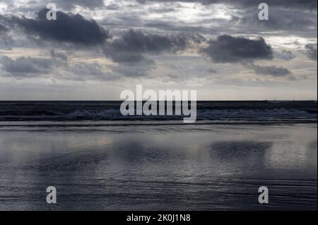 Der nasse Sand reflektiert die Wolken über einem stürmischen Abend an einem Strand der Westküste Neuseelands. Stockfoto