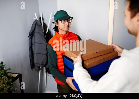 Junger asiatischer Kurier, der Pizza in Pappkartons an den Mann zu Hause liefert Stockfoto