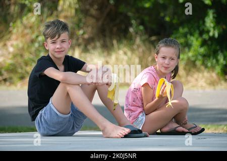 Junge hübsche Teenager Junge und hübsches Mädchen essen leckere reife Banane Naschen im Freien am Sommertag Stockfoto