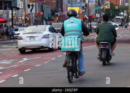 Ein fantuanischer Lieferer auf einem E-Bike in Downtown Flushing, New York. Fantuan 飯糰外賣 asiatische Essenslieferung 法拉盛, 法拉盛華埠, 華裔美國人, 紐約 Stockfoto