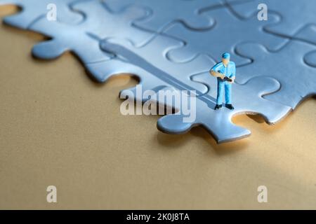 Einzelne kleine Arbeiter Miniatur-Figur am Rand des verknüpften blauen Puzzle. Gelber Papierhintergrund, langer Schatten. Konzept-Hintergrund mit Copy-Space Stockfoto