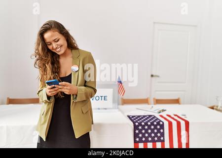 Junge schöne hispanische Frau Wahltisch Präsident mit Smartphone an Wahlhochschule Stockfoto
