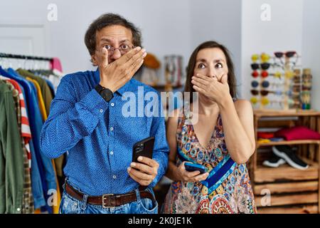 Interracial Paar im mittleren Alter im Einzelhandel mit Smartphone schockiert Abdeckung Mund mit Händen für Fehler. Secret Konzept. Stockfoto